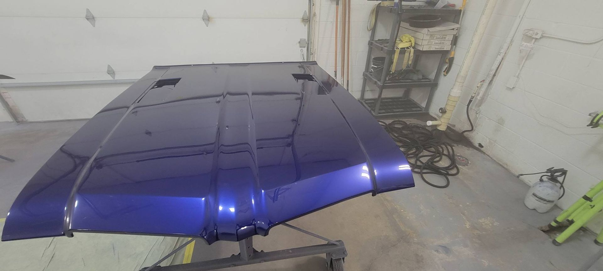 Blue car hood propped open in a garage, reflecting light.