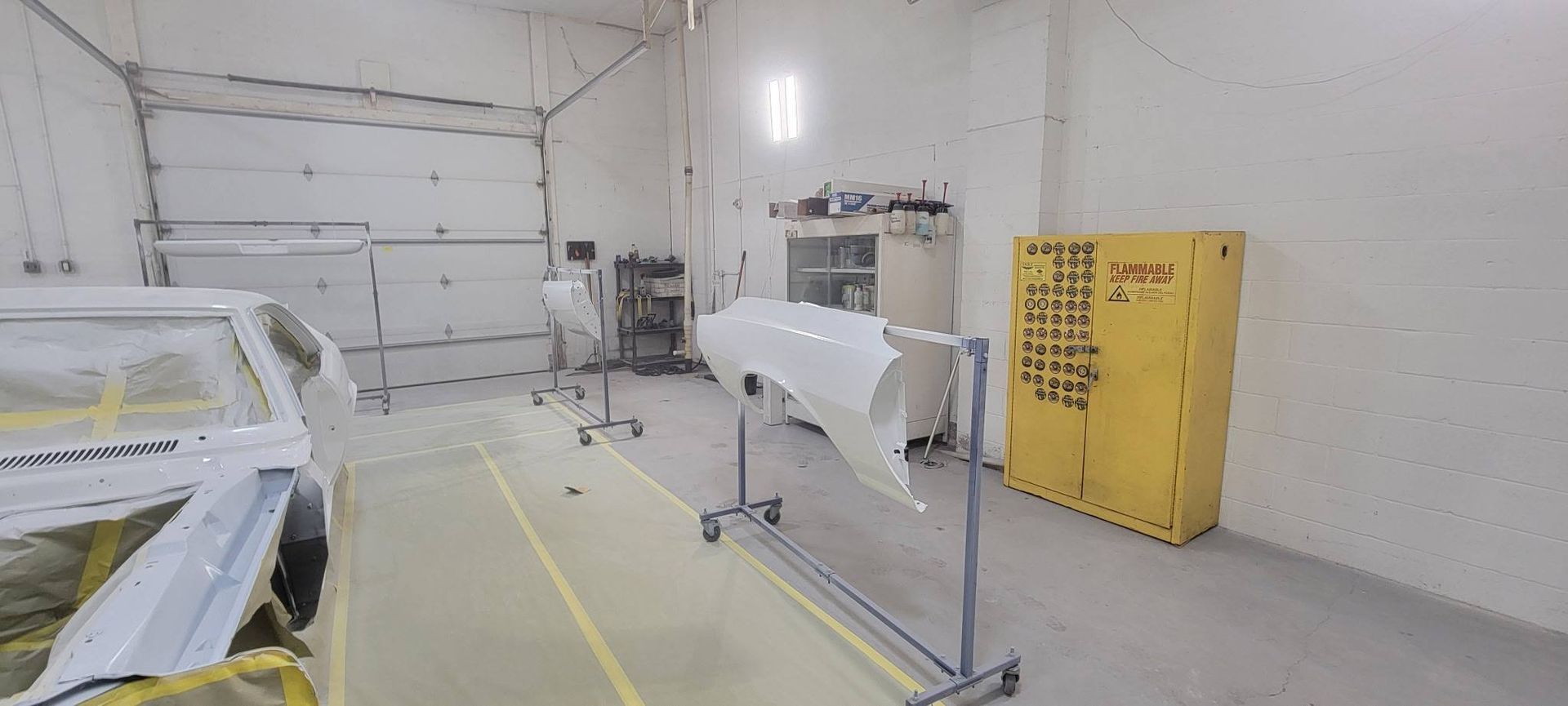 Industrial workshop with white equipment, yellow safety cabinet, and marked floor lines under bright lighting