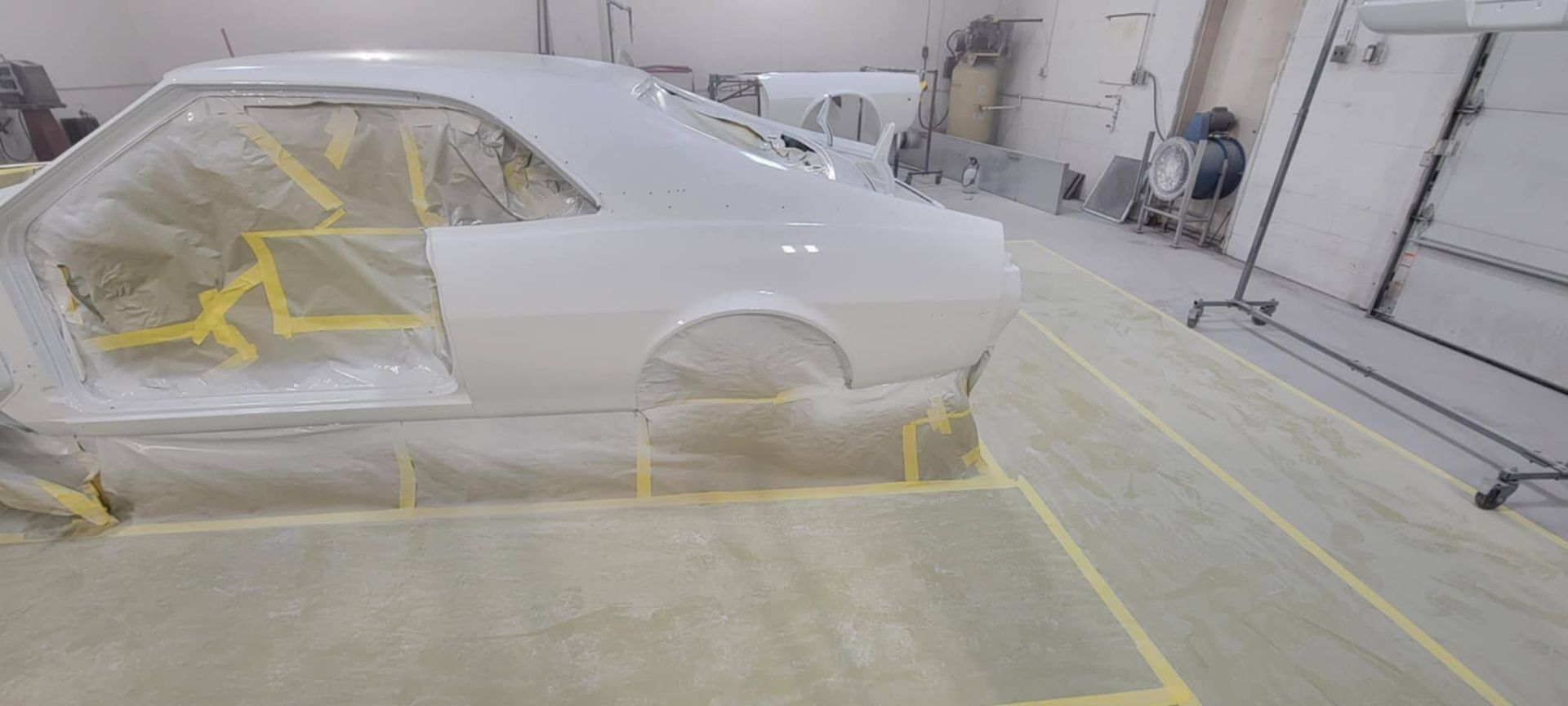 White car body masked with yellow tape inside an auto paint booth