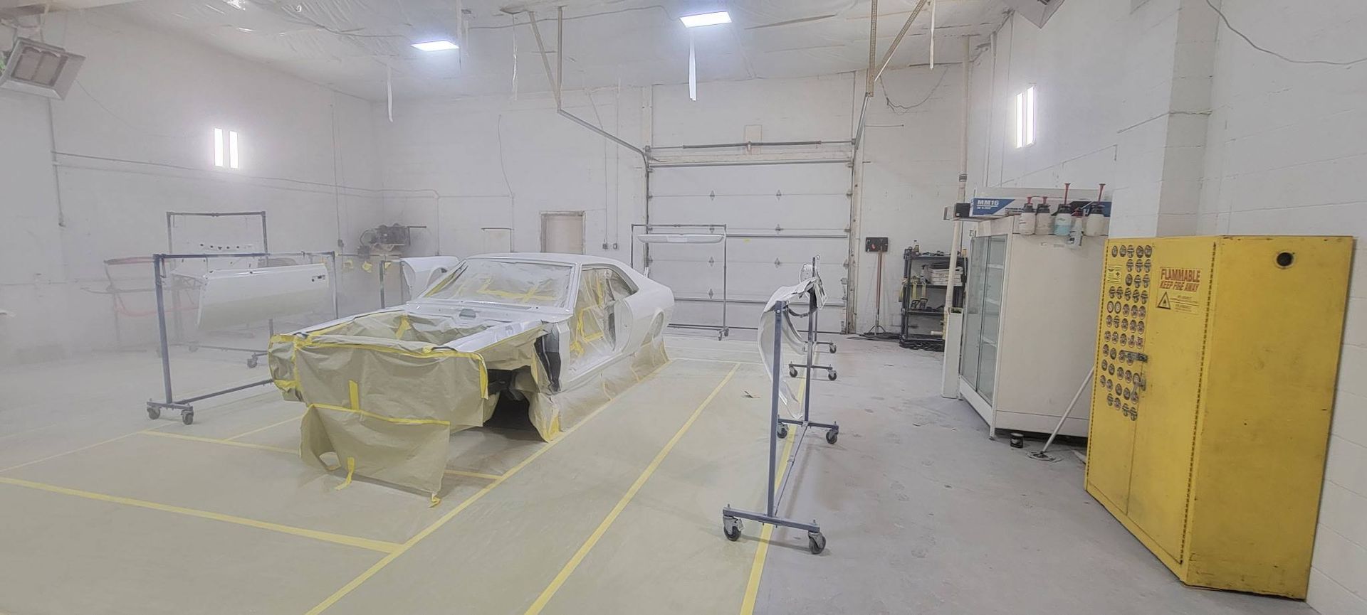 Bright white industrial room with covered equipment, yellow tape on floor, and a yellow cabinet on the right