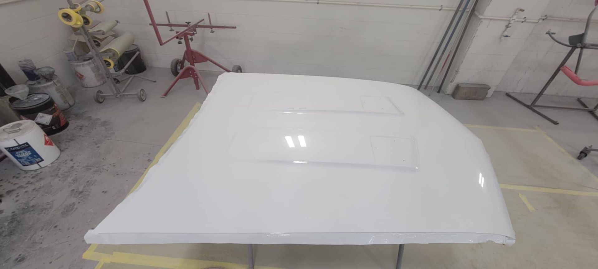 White car roof panel in an auto body repair shop, with a sunroof opening visible