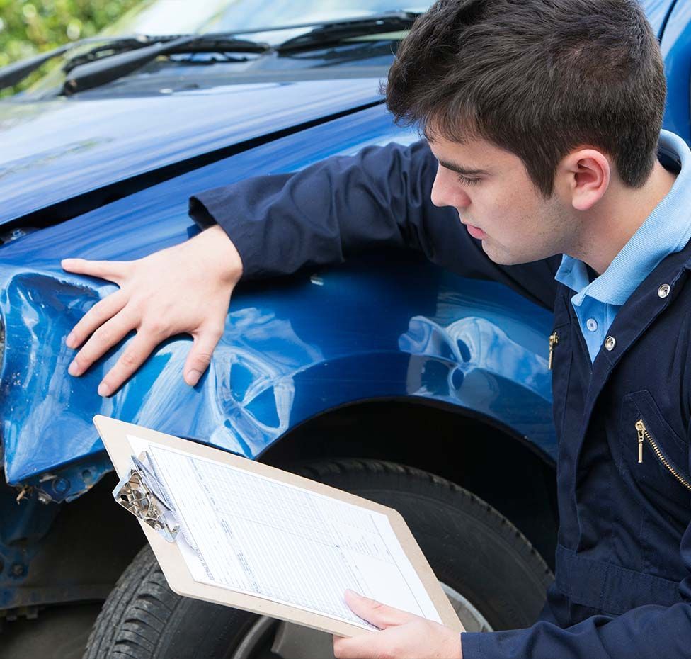 Man inspecting a dented blue car with a clipboard in hand