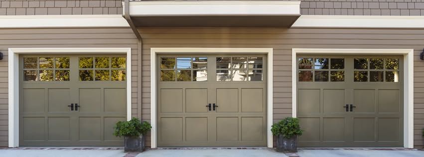 Three beige garage doors on a suburban home with small potted plants on each side