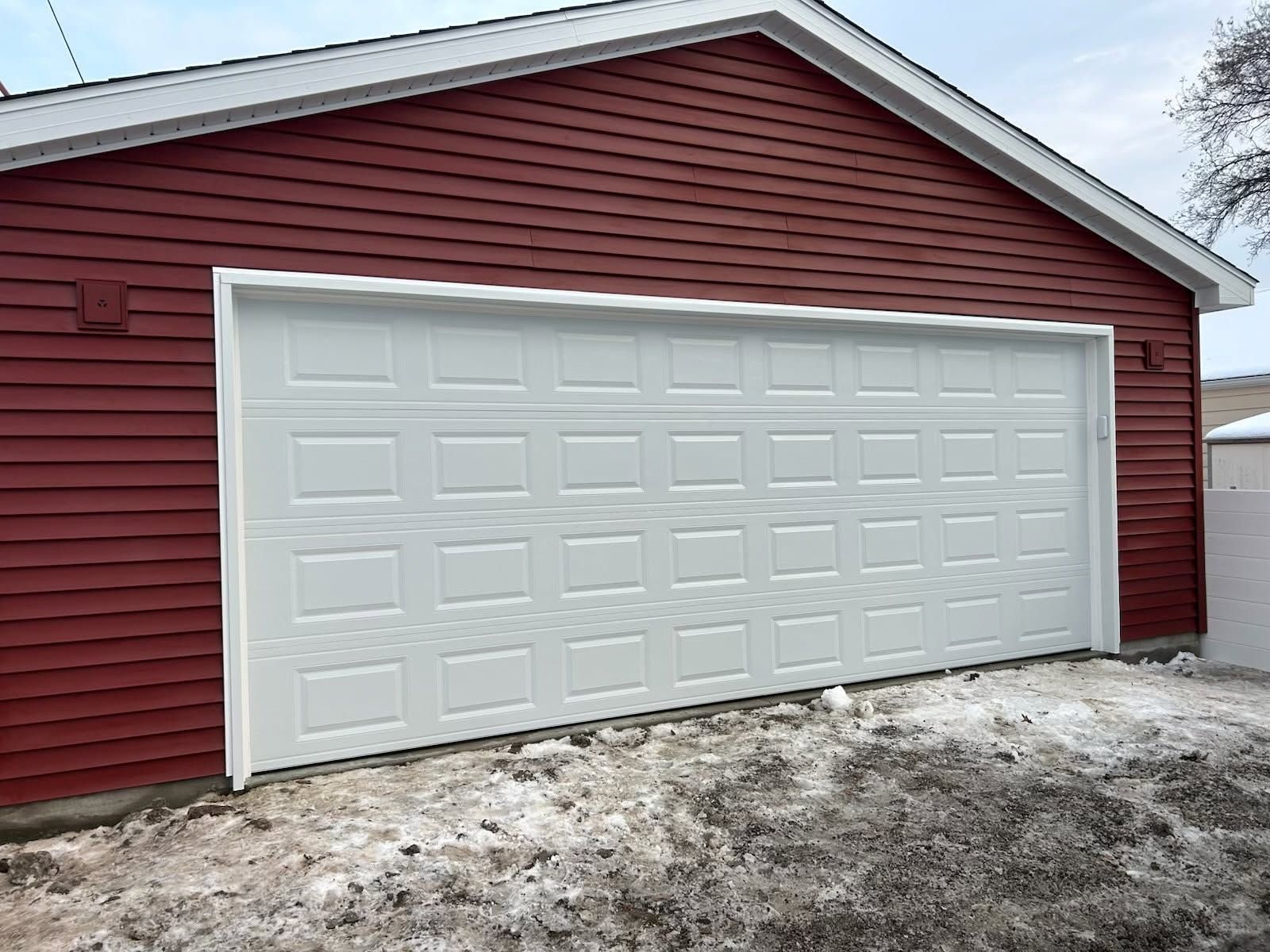 White garage door on a red house with snow on the ground.