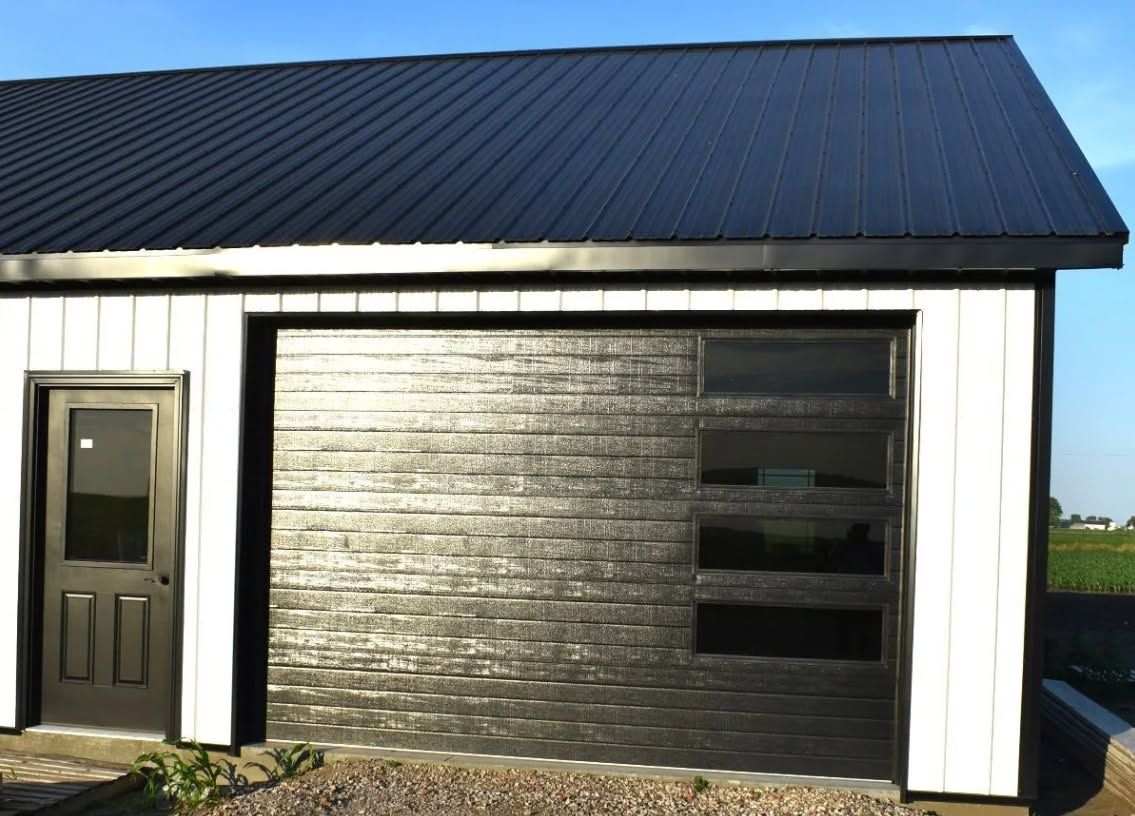 White garage with a dark metal roof and a closed gray door beside a tan entry door.
