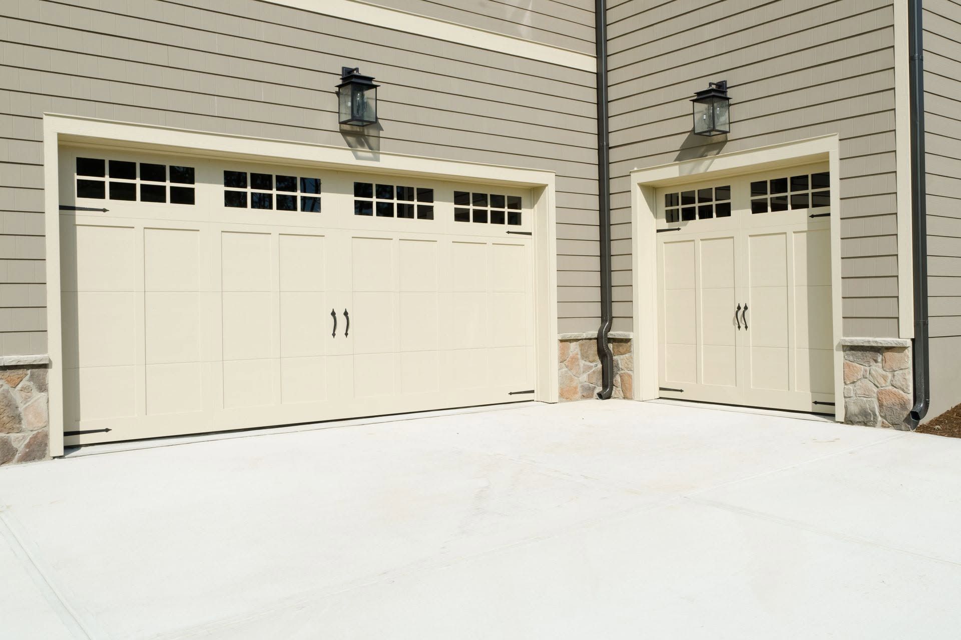 Snow-covered driveway in front of cream-colored garage doors on a house exterior