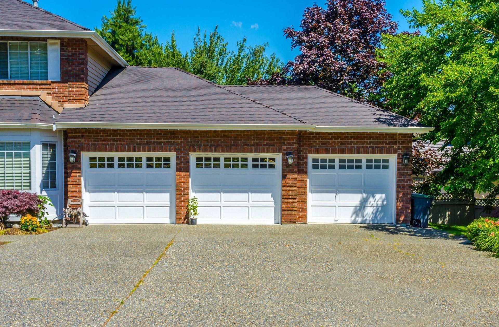 Three-car white garage under brown roof with brick house facade and driveway
