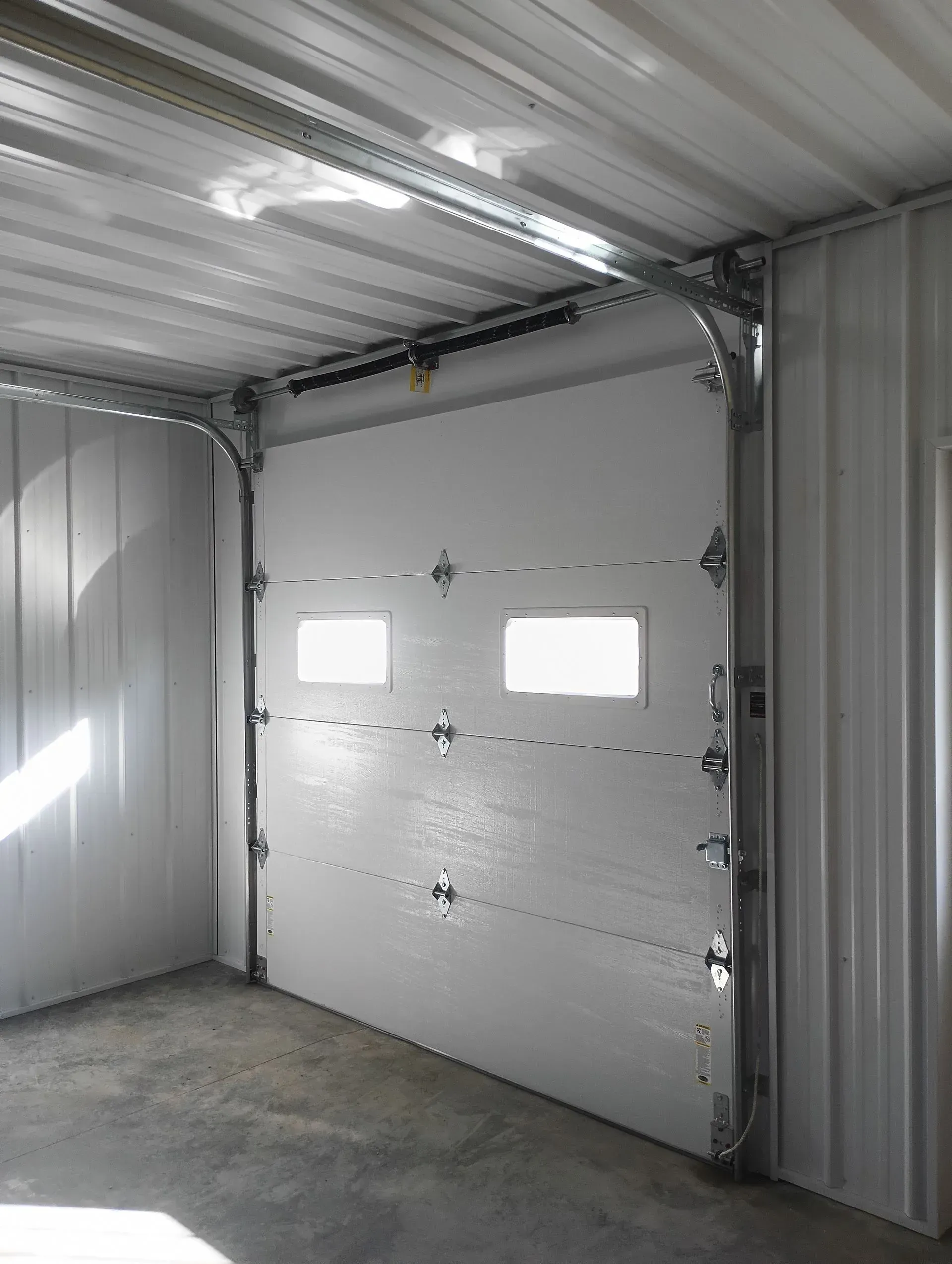 Interior of a metal garage with a closed white roll-up door and concrete floor
