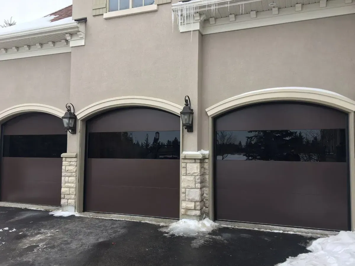Three-car garage with arched beige doors and snow on the driveway