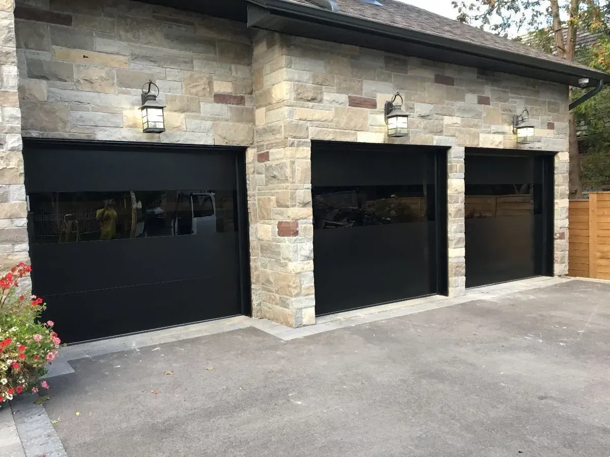 Stone house exterior with three black garage doors and wall lanterns under a dark roof