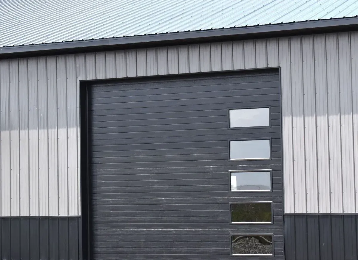 Gray metal warehouse exterior with a large black garage door and narrow windows