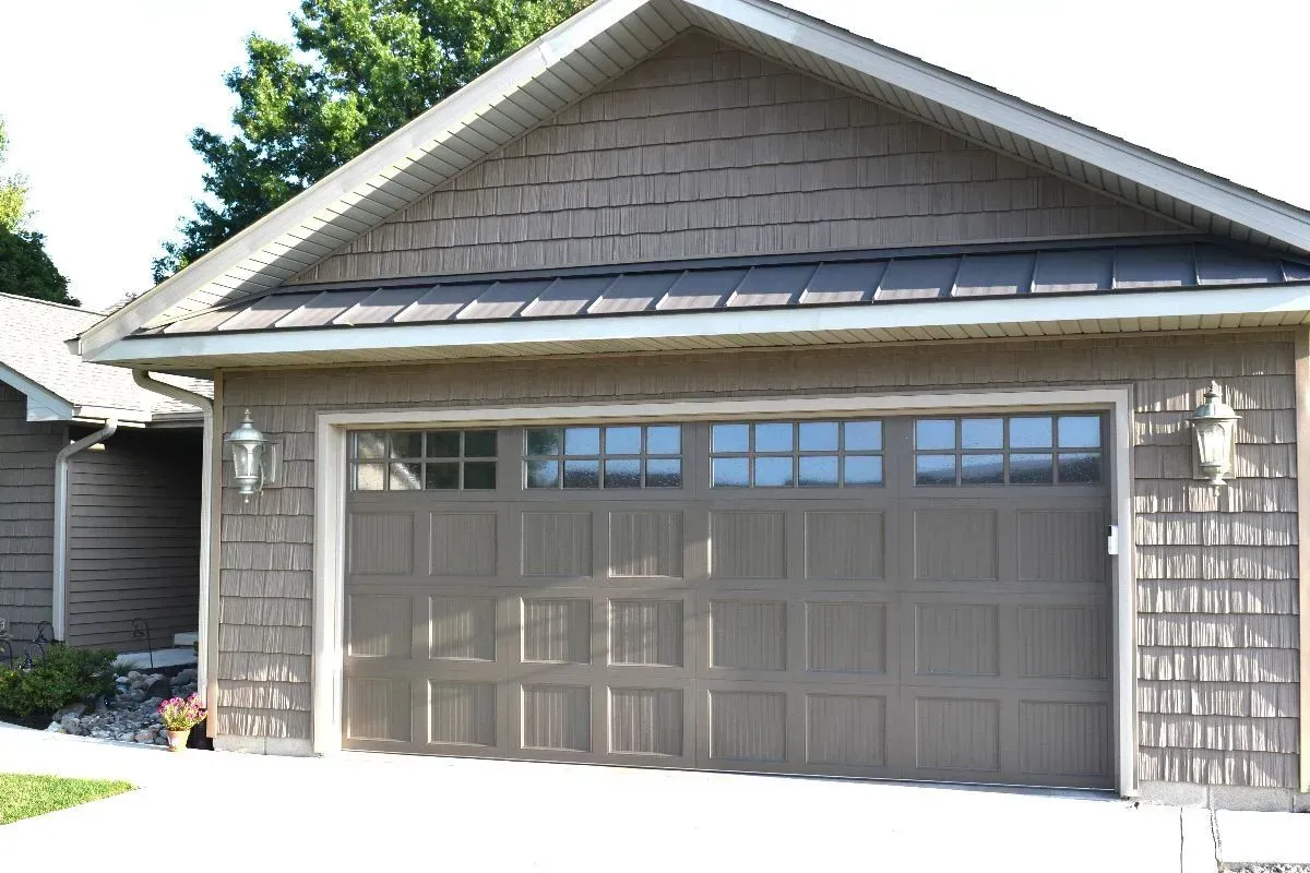 Two-car garage with a brown paneled door and gray shingled siding in bright daylight