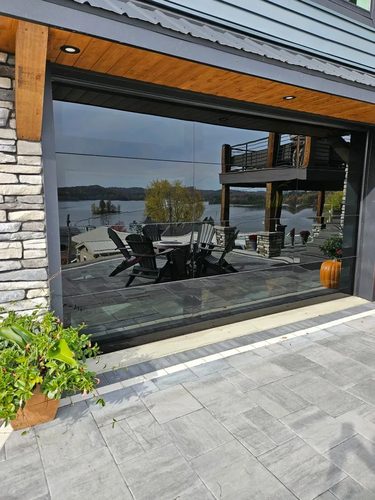 Patio with outdoor dining table and chairs reflected in a large window beside stone and wood siding