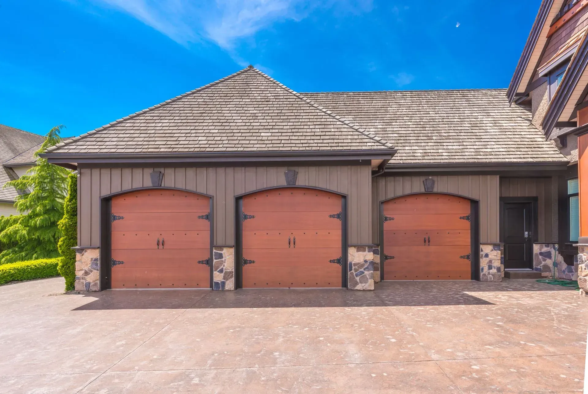 Three-car garage with brown doors and stone accents under a clear blue sky