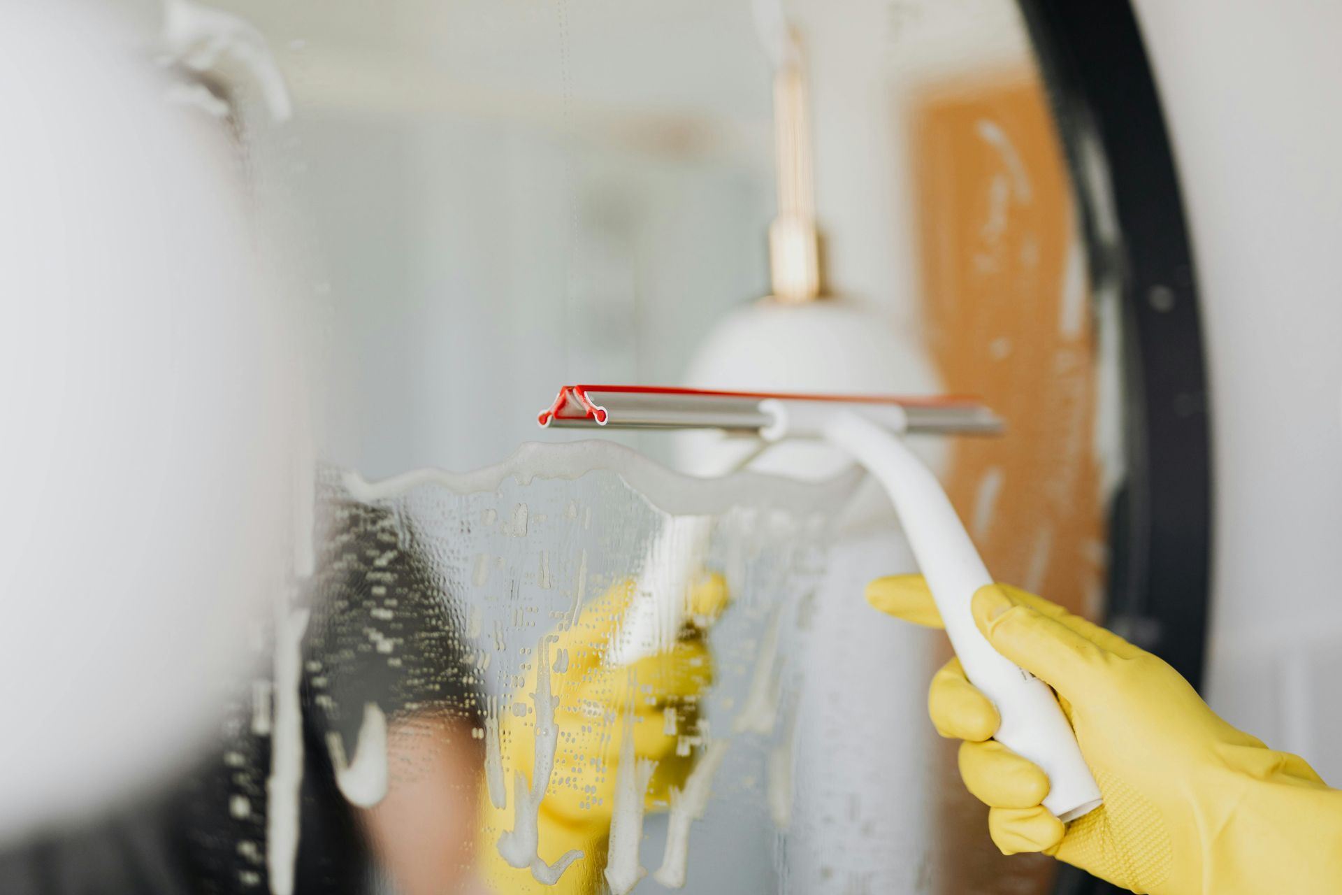 Gloved hands cleaning a foggy bathroom mirror with a white squeegee