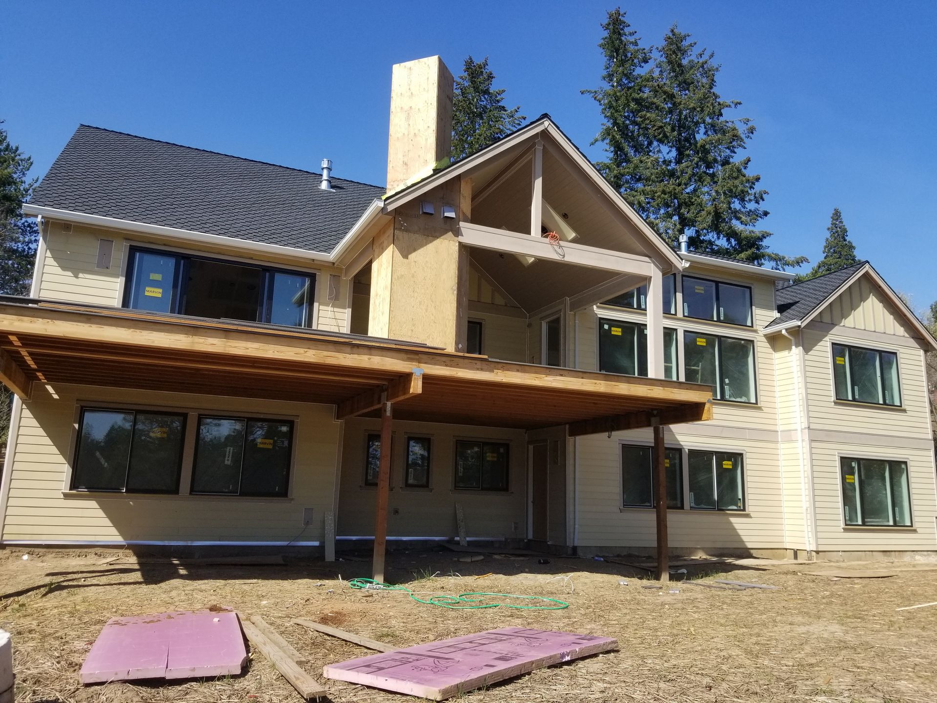 Large beige house with a stone chimney and unfinished wooden deck in a yard under a clear sky