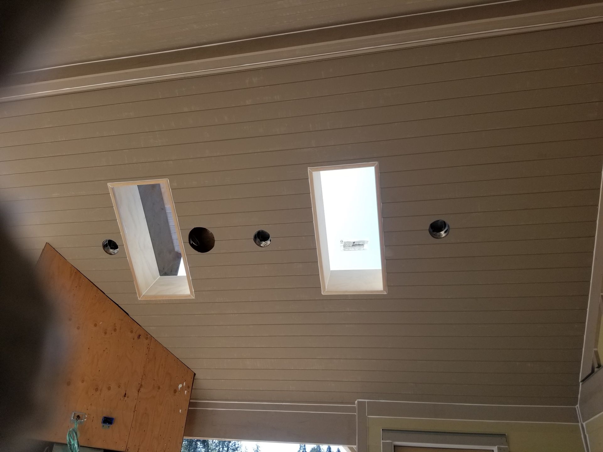 Ceiling with two rectangular skylights and several round holes, partially framed by wood paneling.
