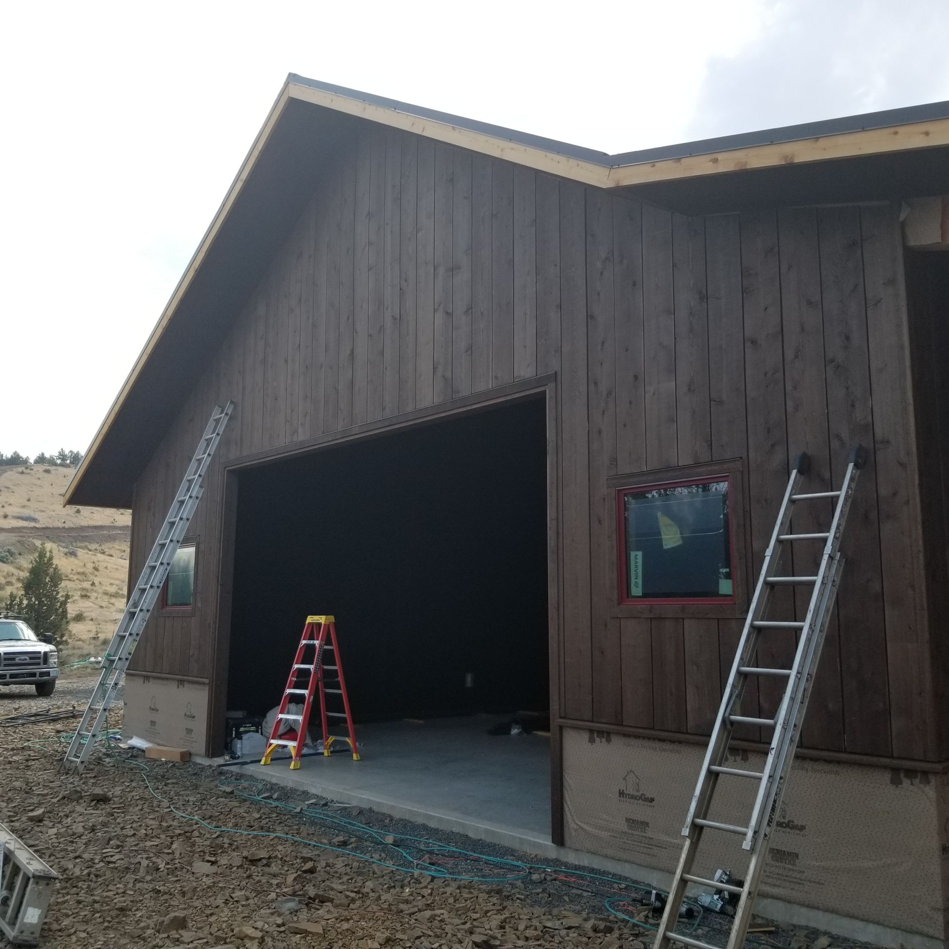 Wood-sided barn with large open garage door and ladders leaning outside and inside
