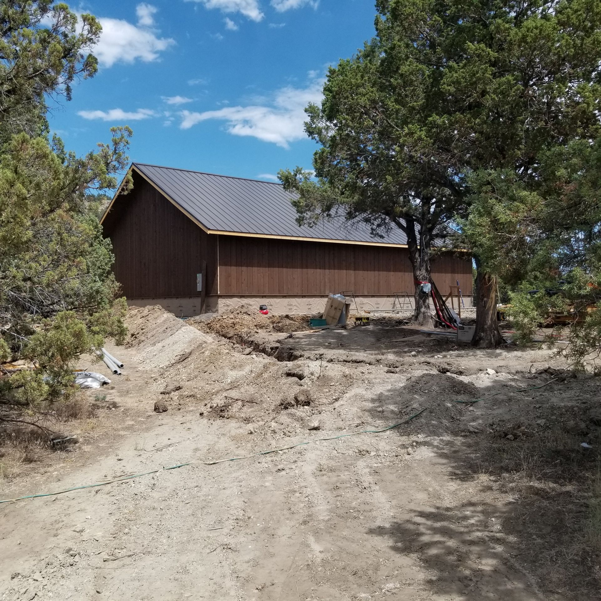 Rural dirt path leading to a wooden barn-like building beside trees under a blue sky
