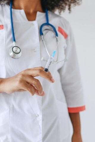 Nurse in white coat holds syringe with a blue liquid, stethoscope around neck.