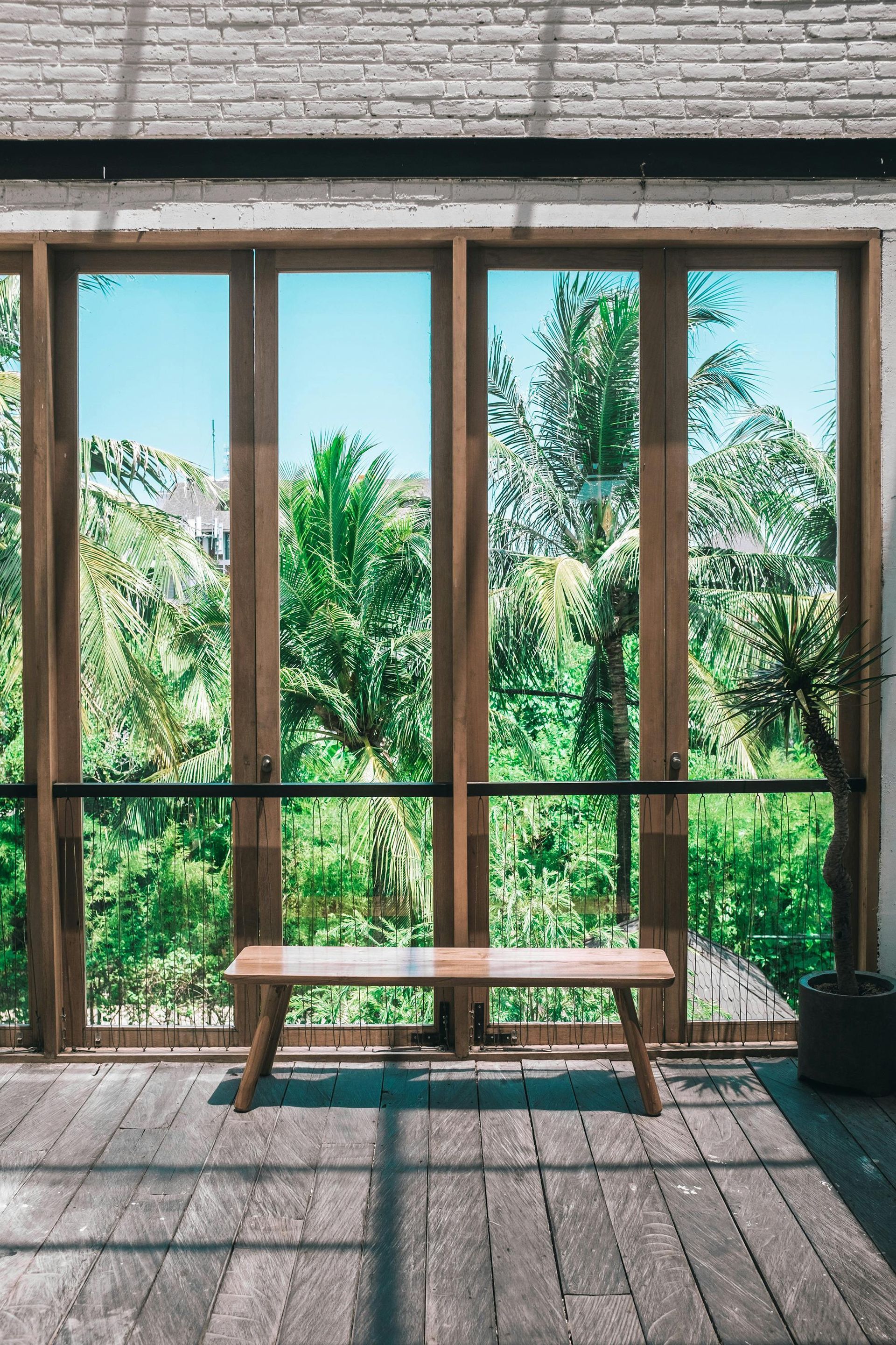 A wooden bench is sitting in front of a large window.