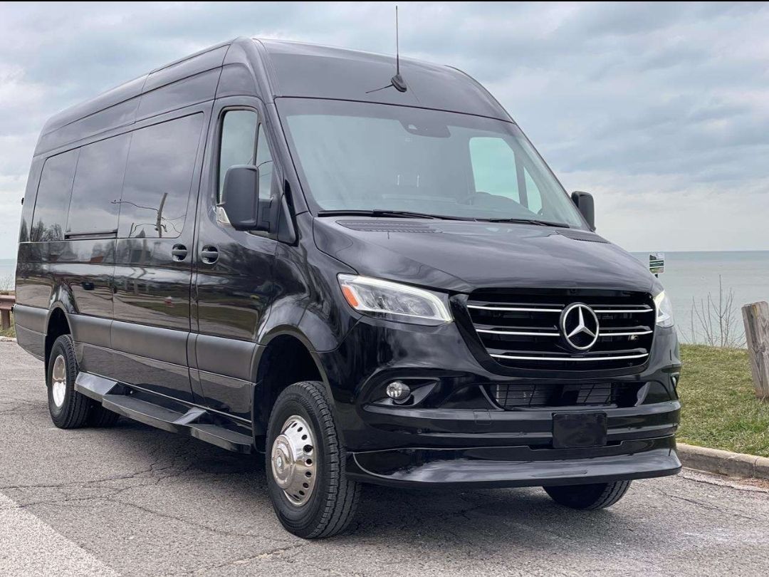 Black Mercedes Sprinter van parked on a paved road next to water.