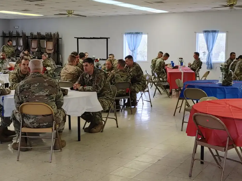 Soldiers in uniform seated at tables, possibly at a gathering in a brightly lit room.