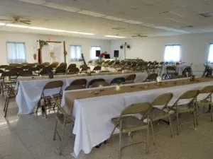 Wedding reception venue: long tables set with white tablecloths, tan chairs, decorations, and a wooden arch.