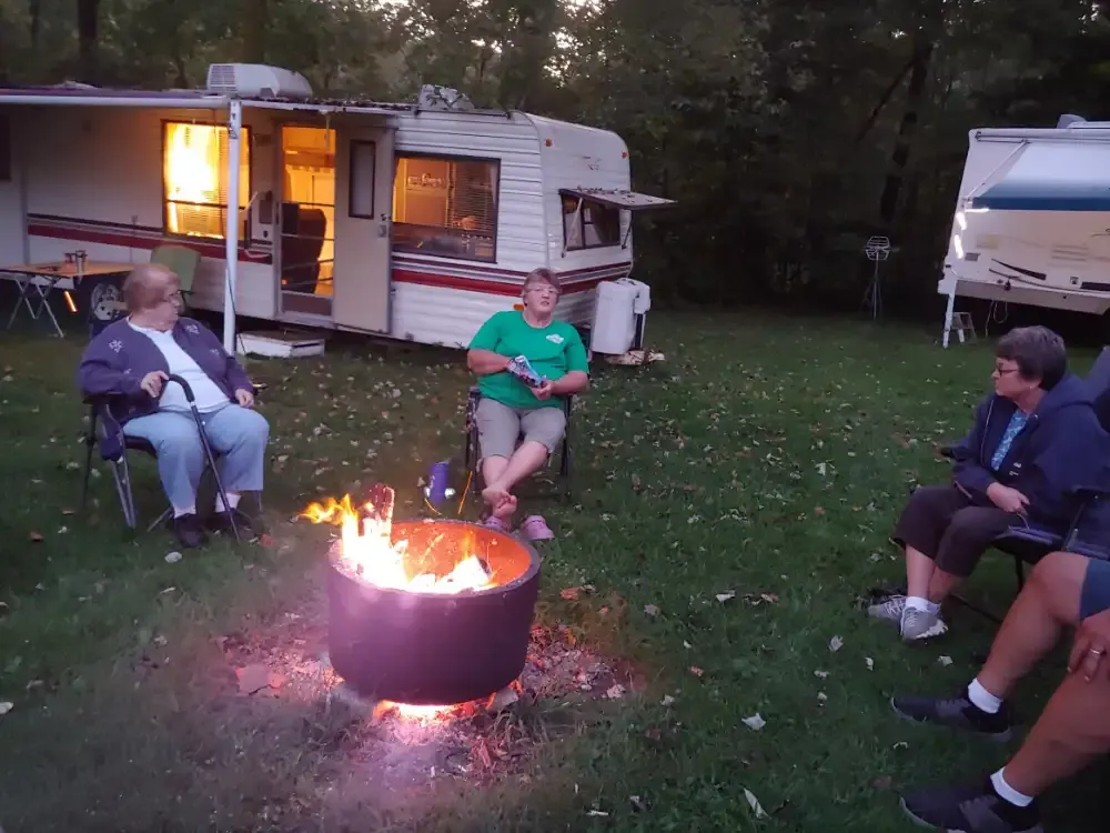 People gather around a campfire near RVs at dusk, chatting.