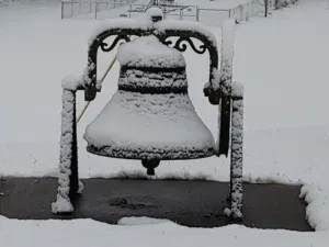 Snow-covered church bell in a snowy landscape.