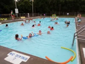 Children playing and swimming in a pool; lifeguard on duty.