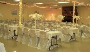 Event hall with rows of tables set with white tablecloths and decorations.