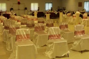 Banquet hall with rows of white-covered chairs, some with pink sashes, set for an event.