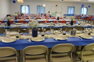 Tables set up in a large room for an event, with blue and red decor and flowers.