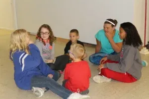 Group of children and an adult sit in a circle on the floor, talking.