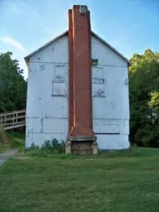 White building with boarded-up windows, red brick chimney, and green grass under a clear sky.