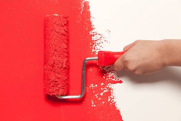 Hand Holding a Paint Roller with Red Color Paint — Jacksonville, NC — C & S Paint Center Hand Holding a Paint Roller with Red Color Paint — Jacksonville, NC — C & S Paint Center