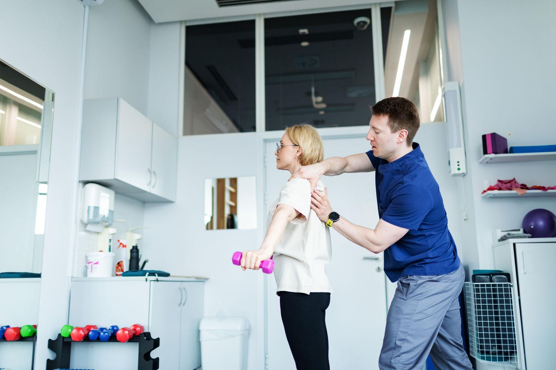 Man helping woman with arm exercise in a bright gym or therapy room
