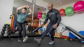 Physical therapist assisting a man with a back exercise on a mat in a bright studio