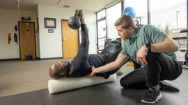 Person bench pressing a barbell in a gym with large windows and mountain views.