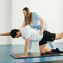 Physical therapist assisting a man in a tabletop stretch on a mat in a bright studio