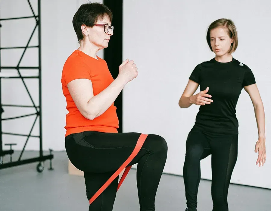 Two people in exercise clothes doing a resistance-band leg exercise in a studio