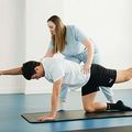 Physical therapist assisting a man in a tabletop stretch on a mat in a bright studio
