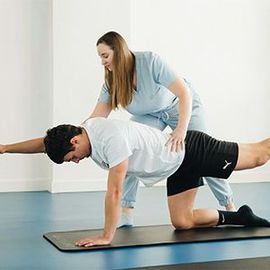 Physical therapist assisting a man with a back exercise on a mat in a bright studio