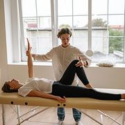 Physical therapist assisting a patient with leg stretch on a treatment table in a bright studio