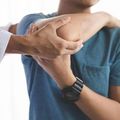 Person stretching an arm while another hand supports the elbow, wearing a blue shirt and black watch.