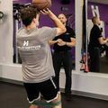 Person shooting a basketball indoors while a trainer watches in a gym mirror.