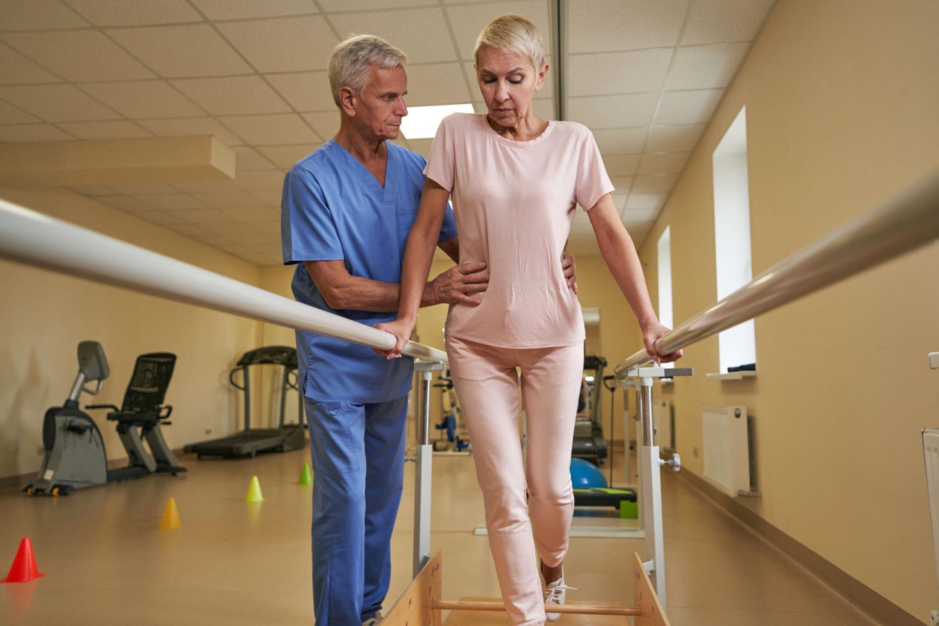 Therapist assisting a patient walking with parallel bars in a rehab gym