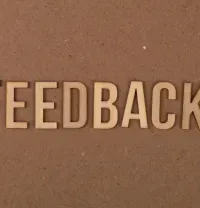 3D letters spelling “FEEDBACK” on a brown textured wall.