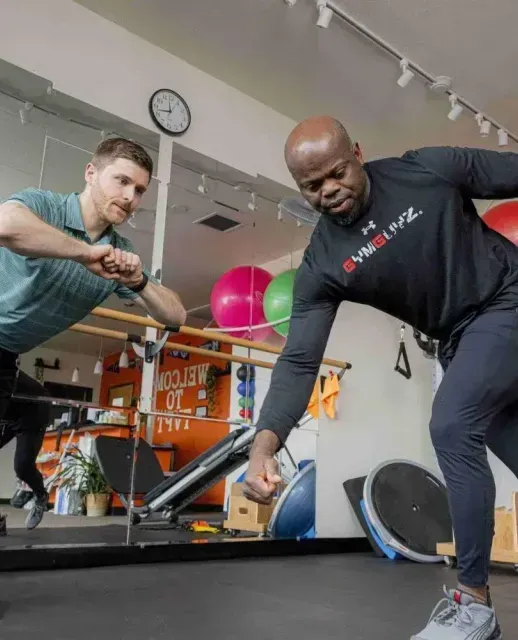 Two people exercising with resistance bands in a gym, one leaning toward a mirror.